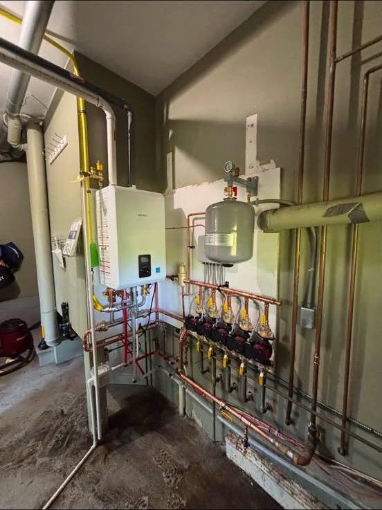 Wall-hung condensing boiler feeding a copper manifold with five zone valves, circulators and an expansion tank