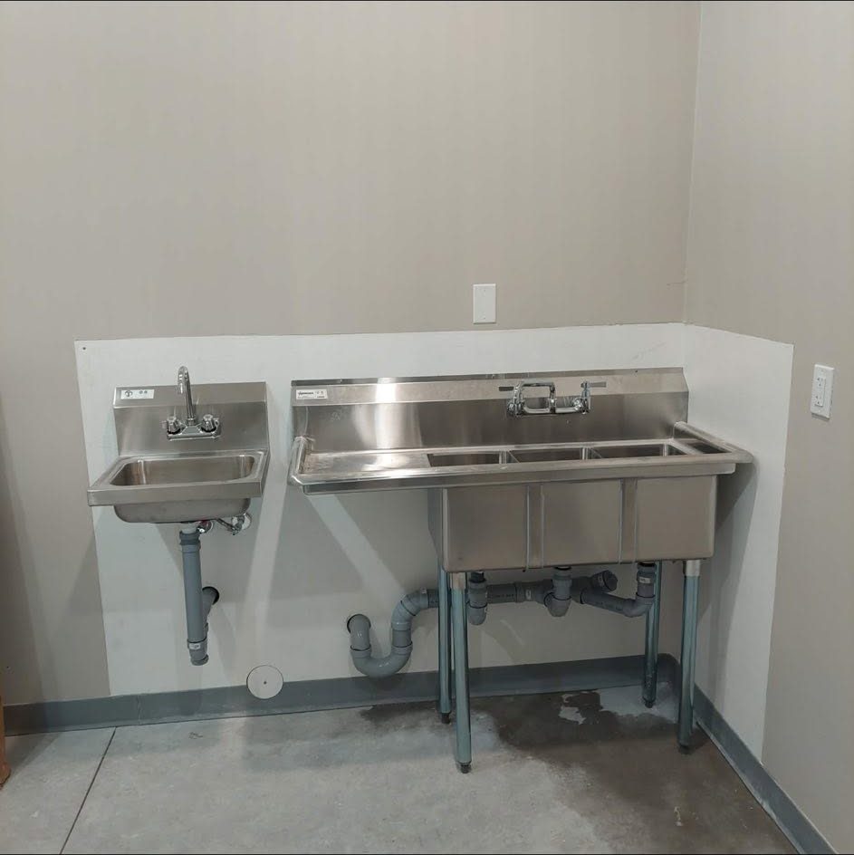 The same commercial sink plumbed in beside a stainless hand-wash basin, with traps, drains and faucets fitted