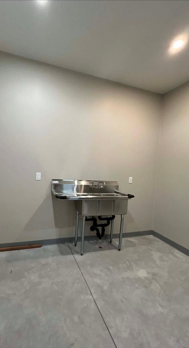 Commercial three-compartment stainless sink standing unconnected in an empty room before plumbing
